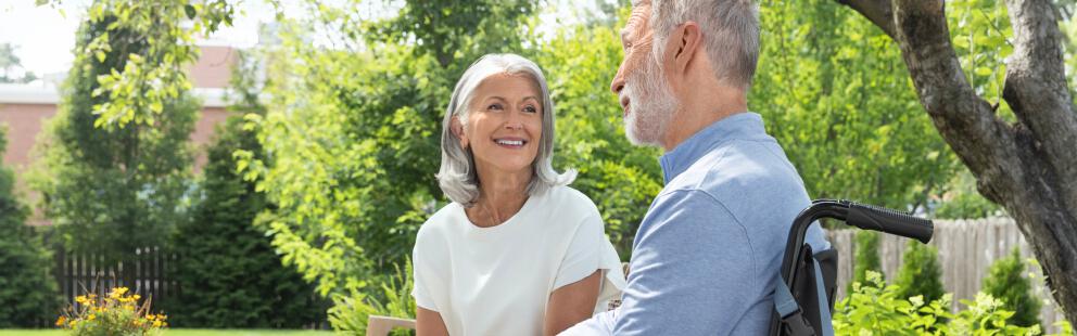 Woman and man in wheelchair with PureWick&trade; Portable Collection System attached sitting outside and smiling