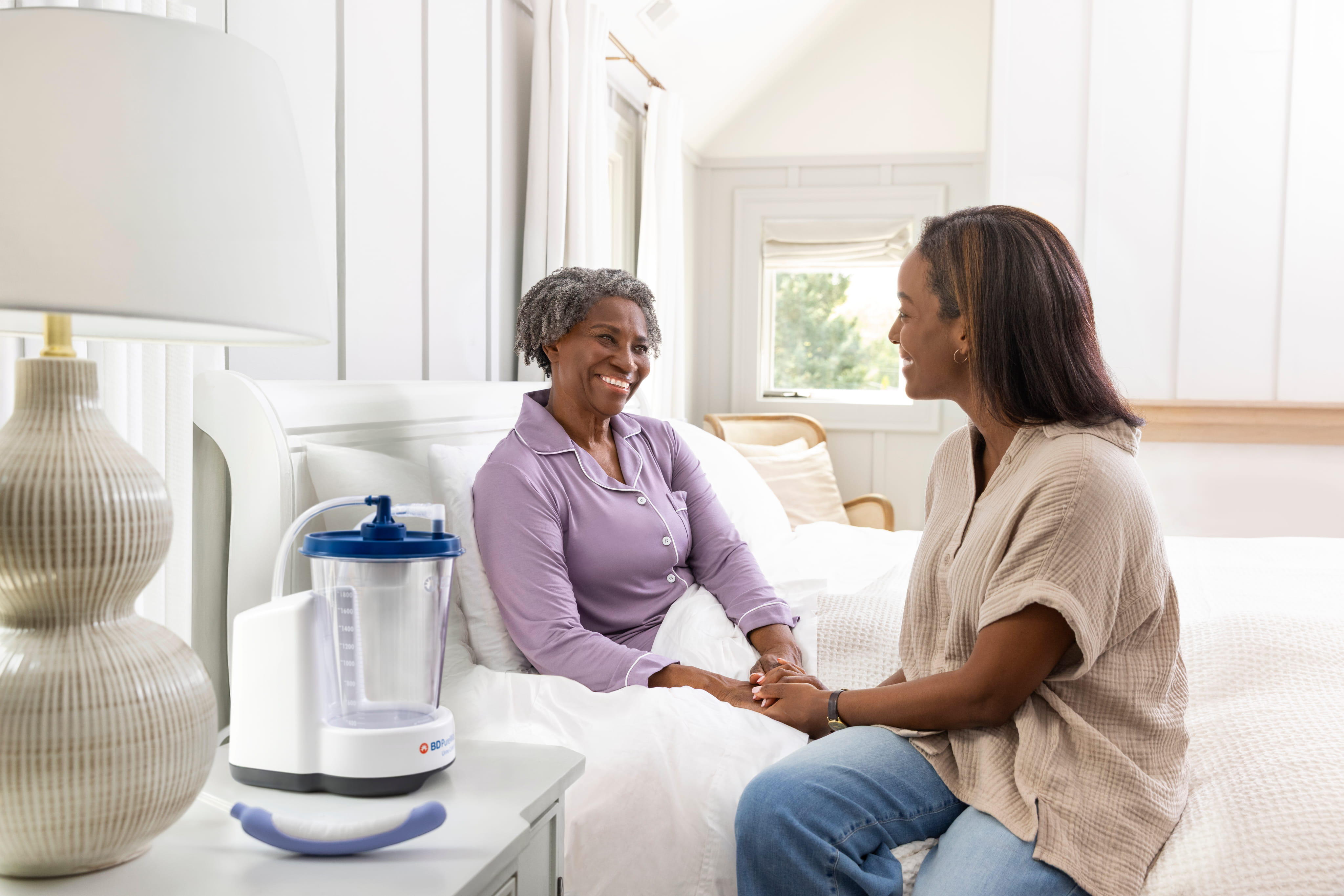 Woman in bed smiling at daughter with PureWick Urine Collection System on nightstand